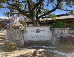Sign displaying Old Town La Verne in front of large oak tree and Warehouse Pizza company